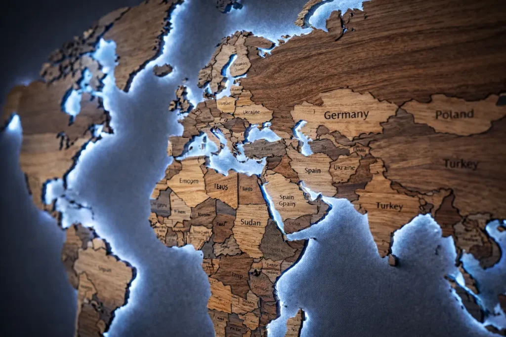 Close-up of 3D LED wooden world map with engraved country names and cool blue LED backlighting on charcoal wall.
